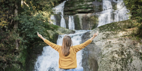 cropped-1763379110-web_version-frau_sitzt_vor_wasserfall_mit_ausgebreiteten_armen_querformat_allgaeu_gmbh__angel_galan_medina